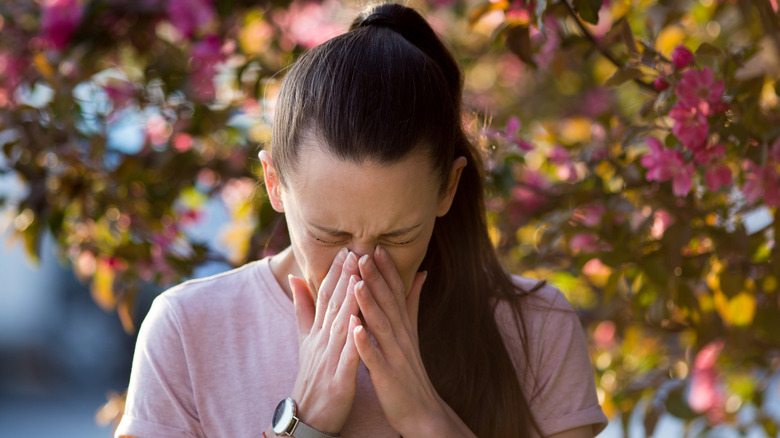 Woman sneezing into tissue in front of tree