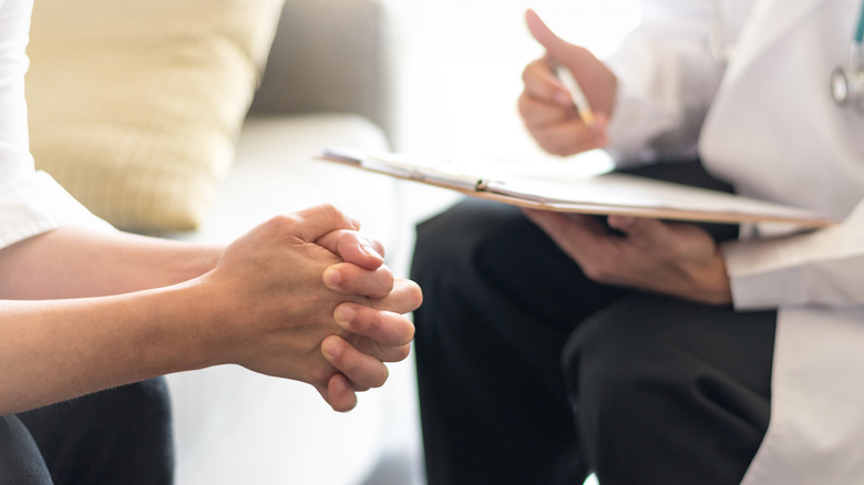 Doctor holding pen and clipboard talking to someone with their hands together