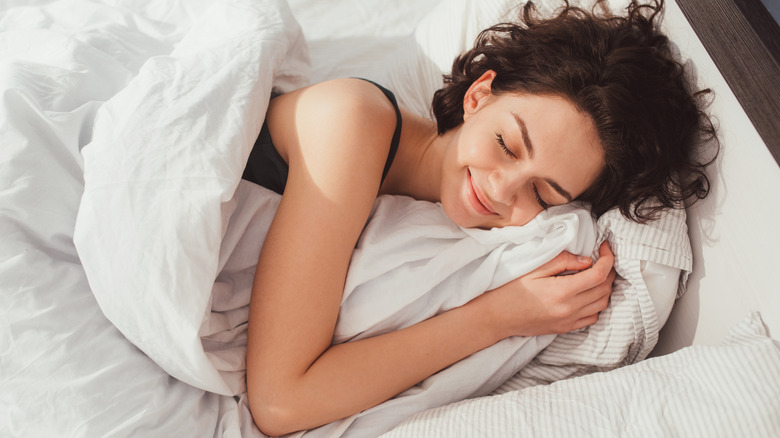 Woman in bed, smiling, with eyes closed
