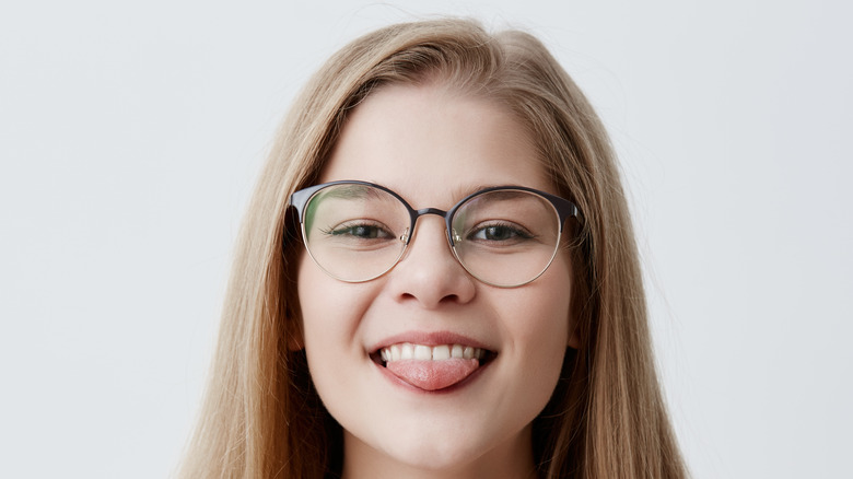 Young girl in glasses sticking out tongue against her teeth