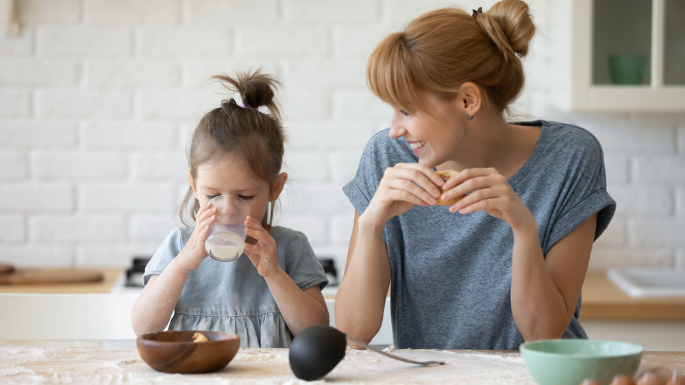 Young girl drinks a glass of milk while mom watches