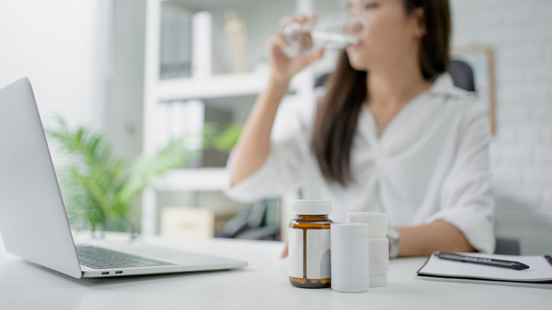 A woman drinks water next to several pill bottles