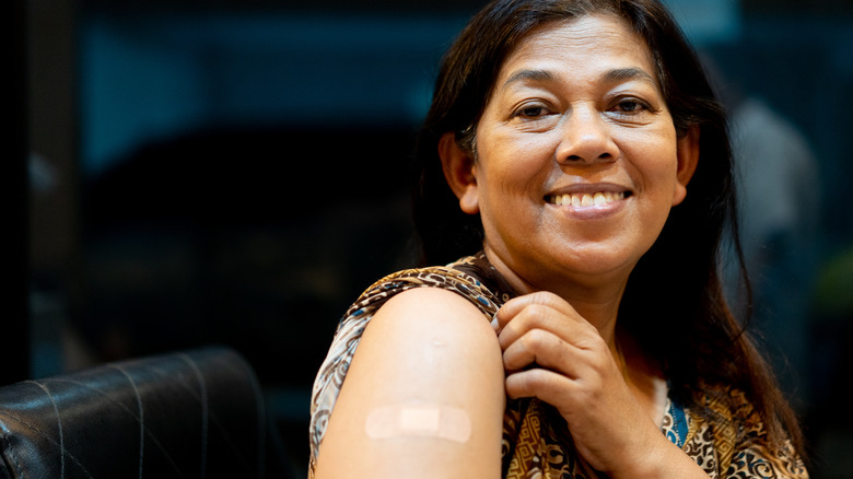 A smiling woman shows the bandage on her arm after vaccination