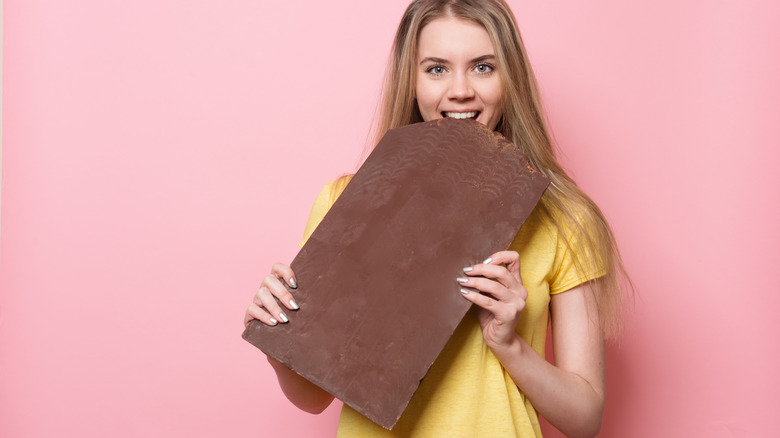 Woman holding and eating giant chocolate bar