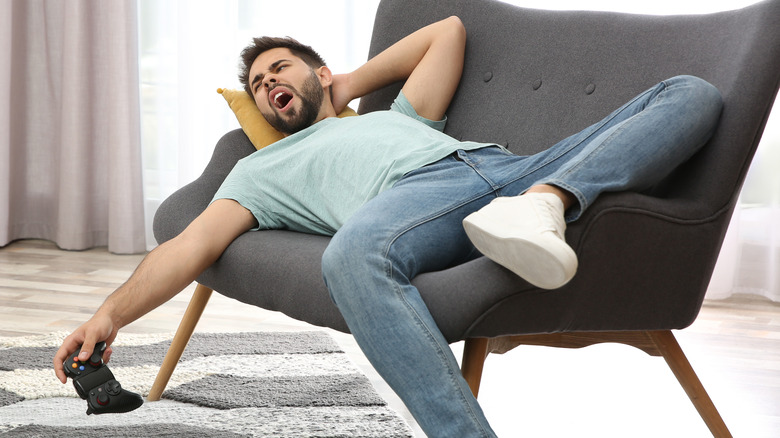 Man laying on couch while yawning, with video game controller in hand