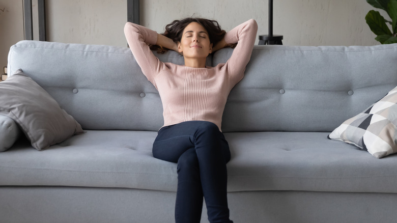 Woman lounging on couch with her eyes closed and hands behind her head