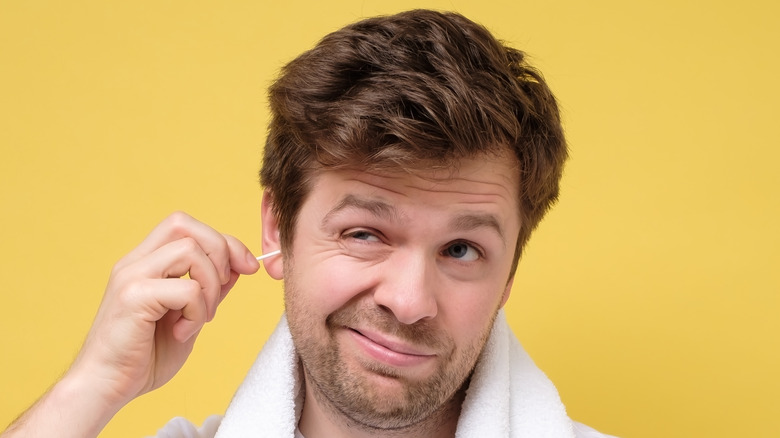man using cotton swab to clean earwax