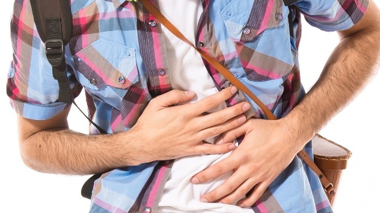 Man wearing headphones, sunglasses, backpack, and picnic basket clutching his stomach in discomfort