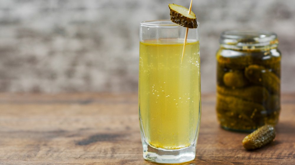 Pickle juice in glass and a can of pickled cucumbers on wooden table background