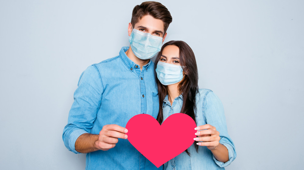 Masked couple holding pink heart