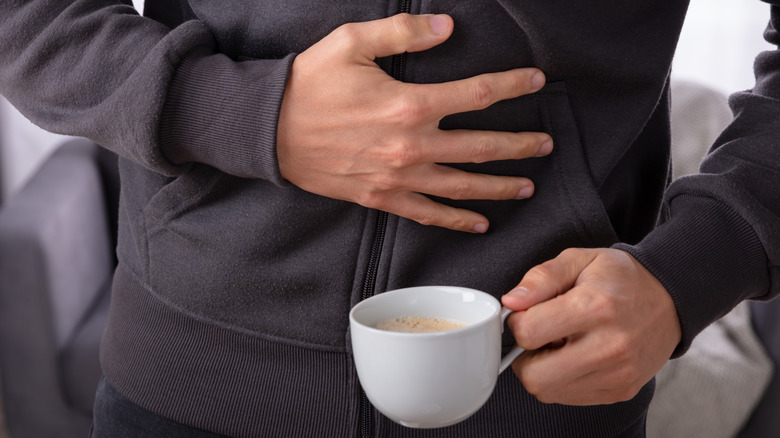 sick man holds coffee in one hand, stomach with the other