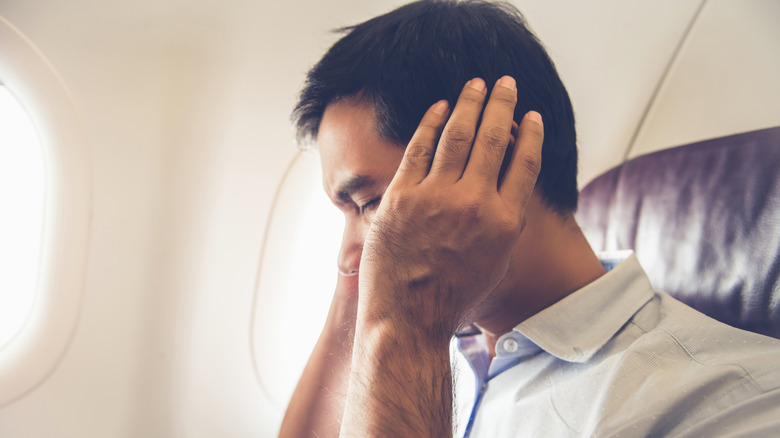 A man holding his ears in pain while on a plane