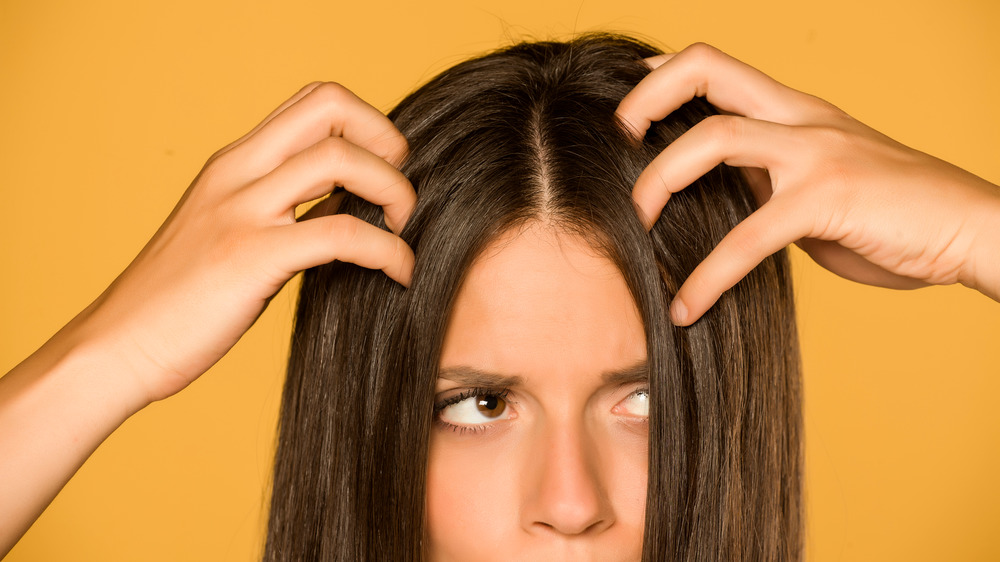 A woman scratching her hair with an all yellow background 