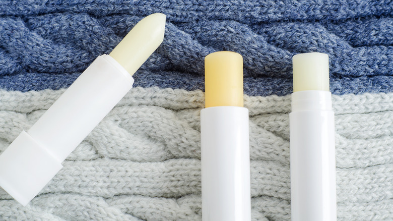 Three sticks of lip balm on a knitted material background