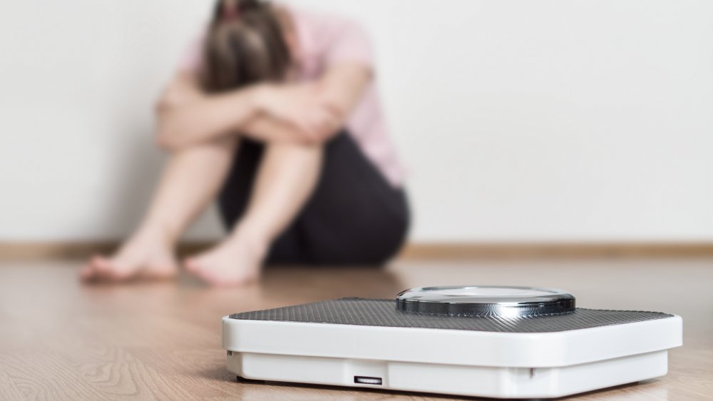 Scale and depressed, frustrated and sad woman sitting on floor 