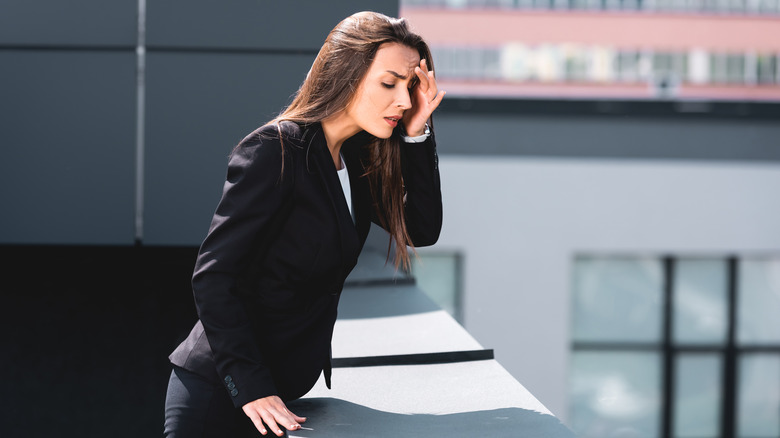 Woman looking down from rooftop with hand on head