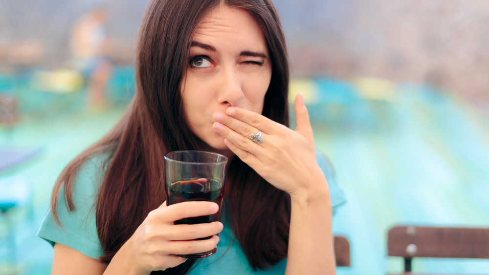 Woman drinking soda and covering her mouth while burping