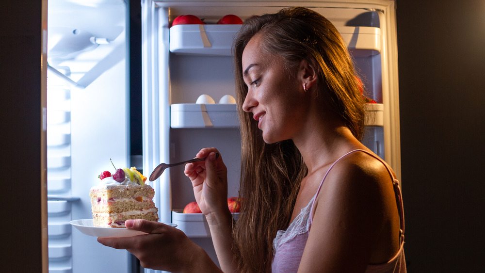 Woman in front of open fridge eating cake