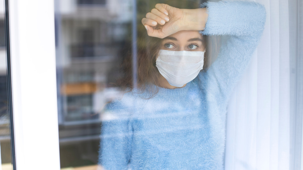 woman in face mask looking out a window
