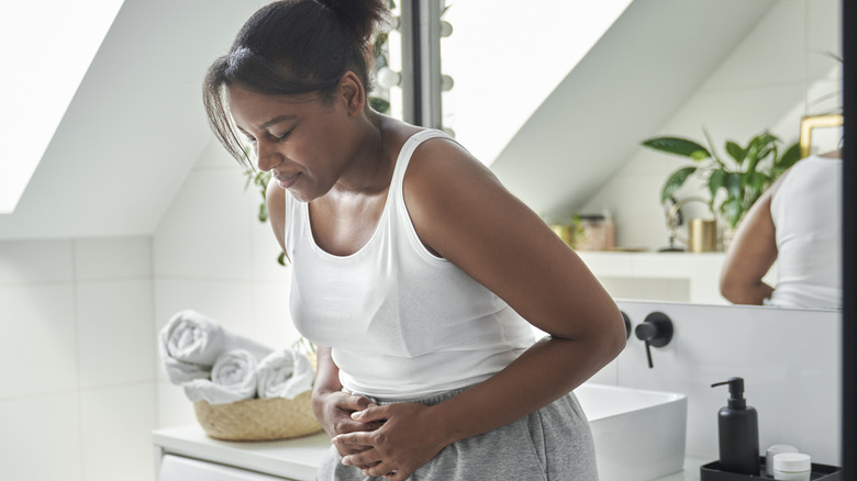 Pained woman holding stomach in bathroom