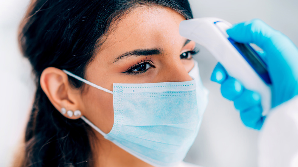 Stock photo of a woman in a face mask getting her temperature checked via her forehead