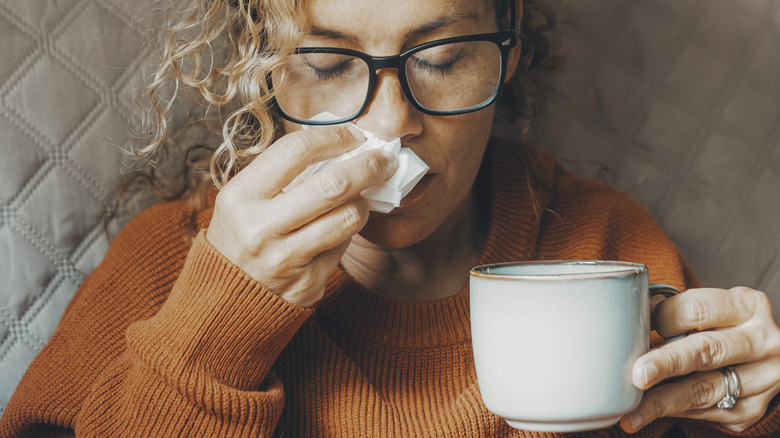 woman with tea who is blowing her nose