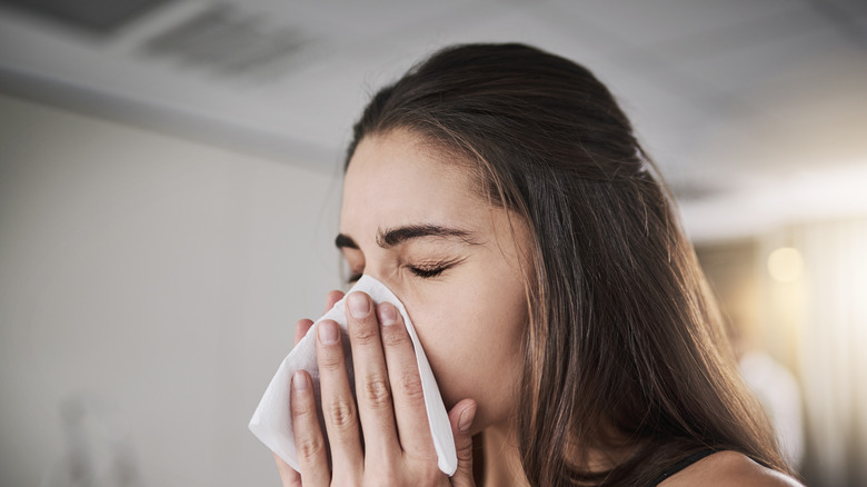 young woman blowing her nose into tissue