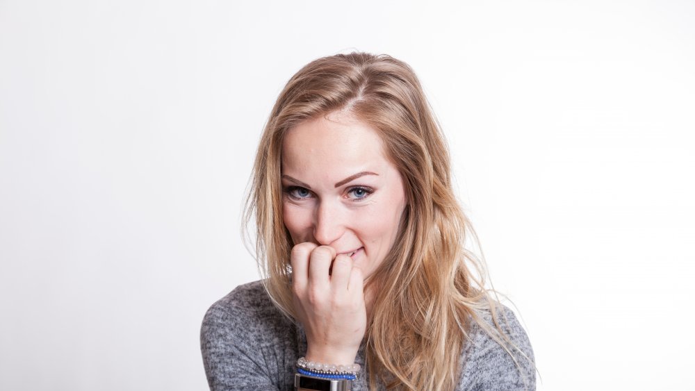 portrait of an embarassed blond woman chewing nails due to her nervousity