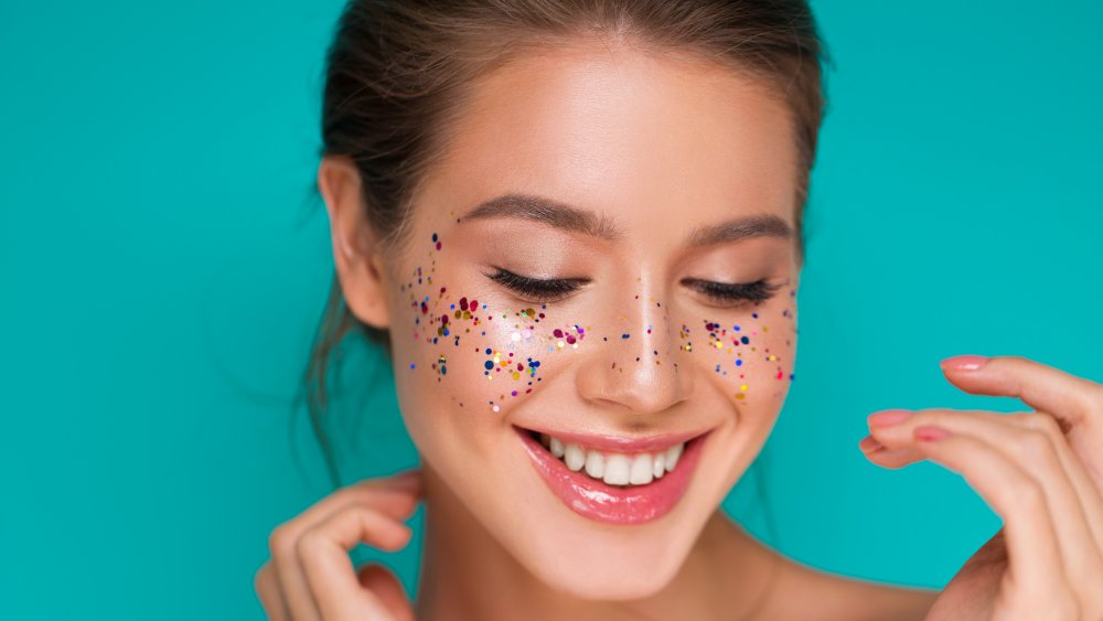 Woman with glitter on her cheeks blushing with blue green background