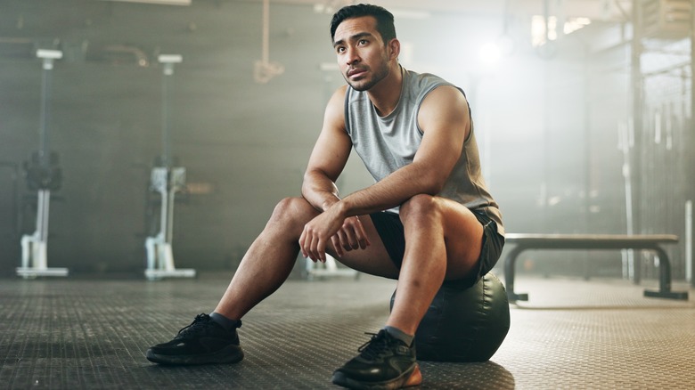 man sitting on a medicine ball at the gym