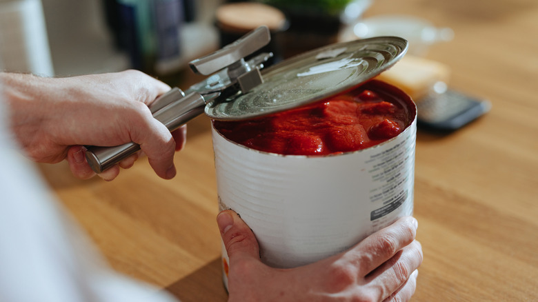 A man's hand opening a can of tomatoes using can opener