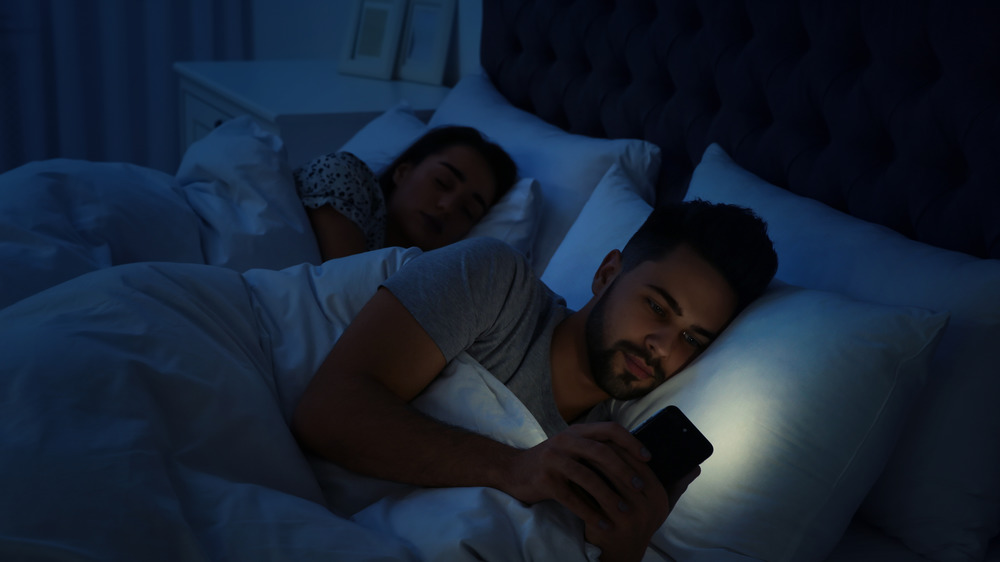man in dark in bed looking at phone