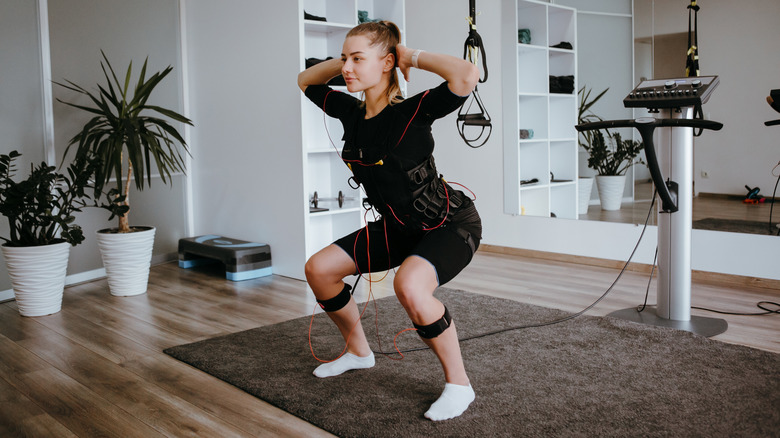 Girl doing prisoner squats in suit with cables