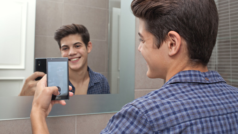 A teenage boy takes a selfie in the mirror