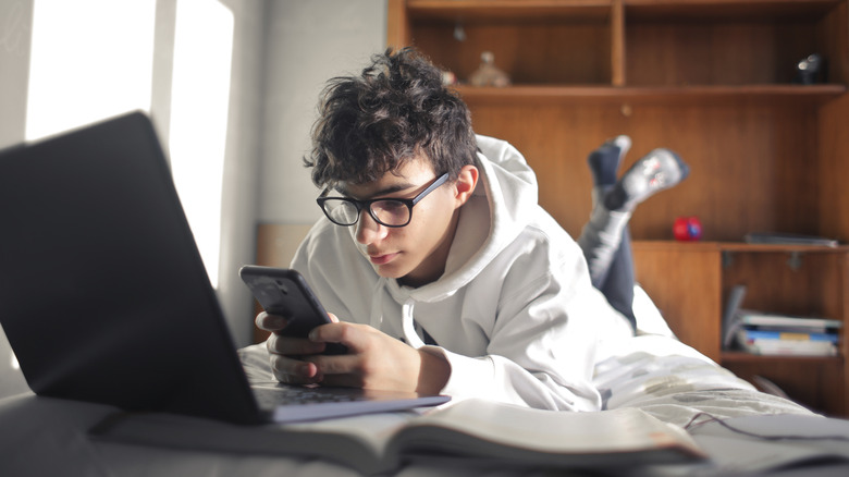A boy looks at his phone and computer