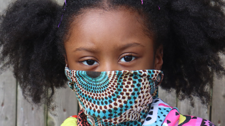 Young girl wearing cloth mask against a fence