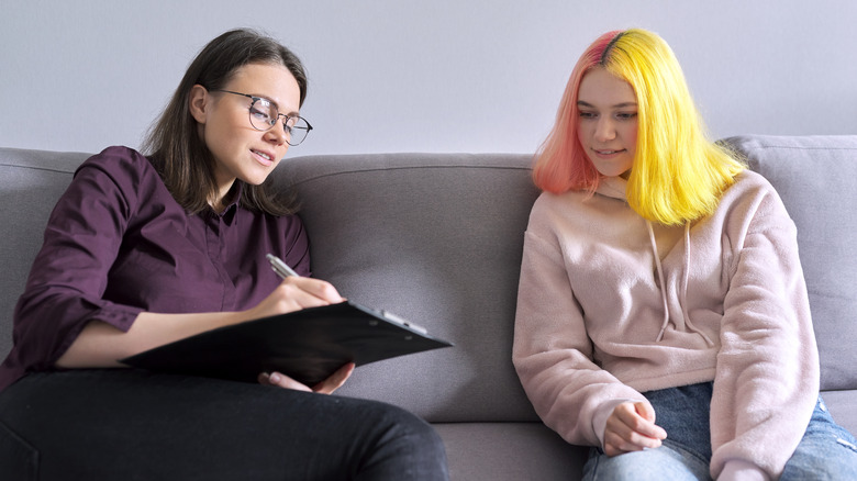 Therapist sits on couch beside teen girl patient
