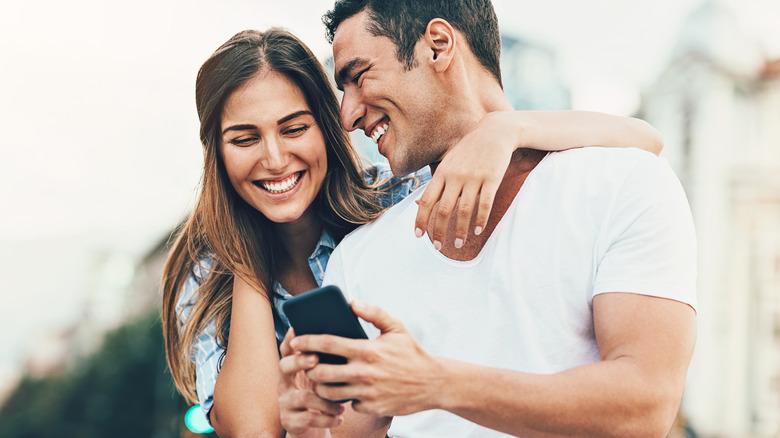 Attractive couple smiling and checking phone
