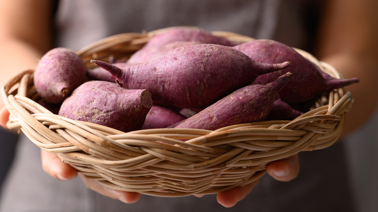 A woman holding a basket of purple root crops