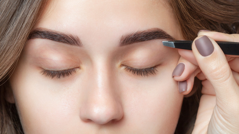 Plucking eyebrows with tweezers