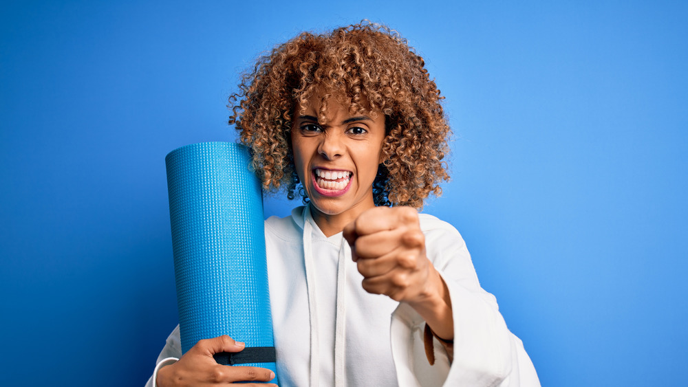 Woman holding up a fist and a yoga mat