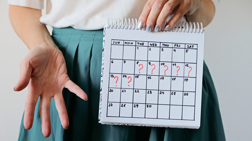 Confused woman holding up a calendar trying to track her period 