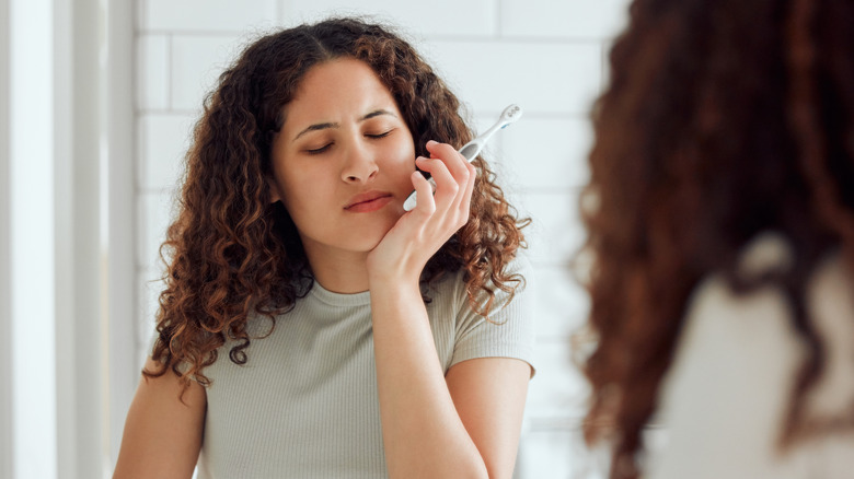 A woman holding her sore jaw and a toothbrush