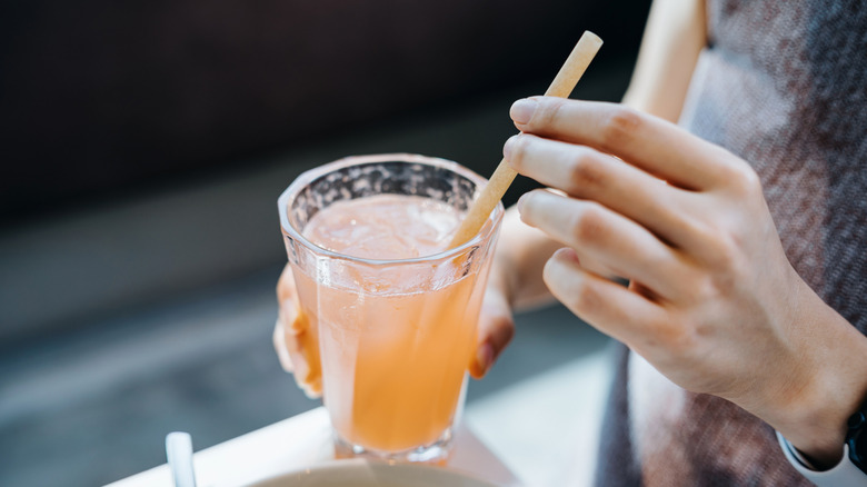 A woman's hand using a straw in a citrus juice drink