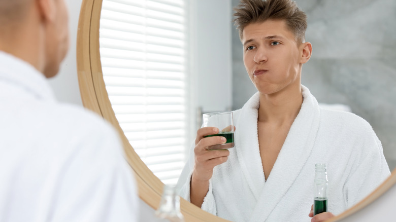 A young adult man looking in the mirror while using mouthwash