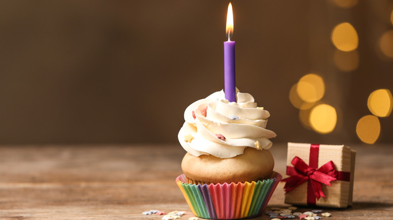 A cupcake with a lit birthday candle and a present sitting next to it
