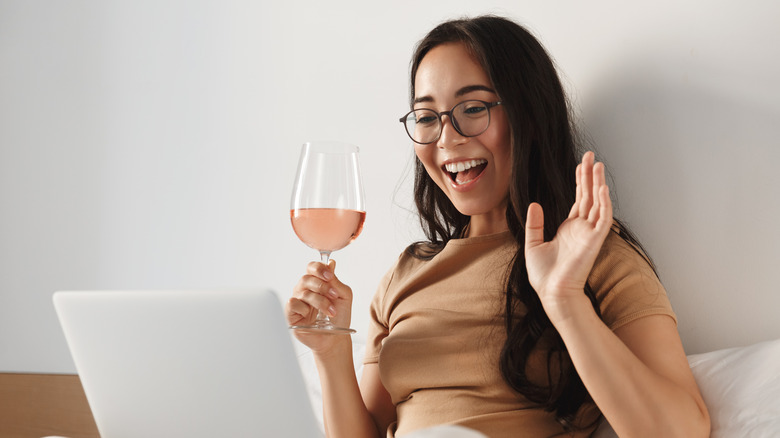 Woman holding glass of wine while talking into her laptop