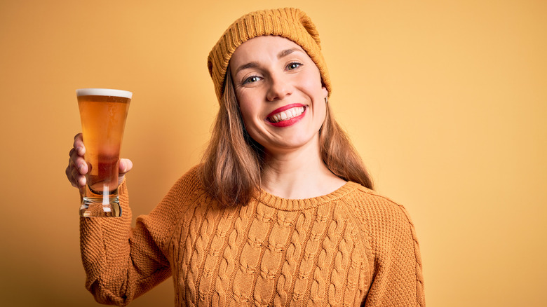 smiling young woman clad in all yellow holding a beer 