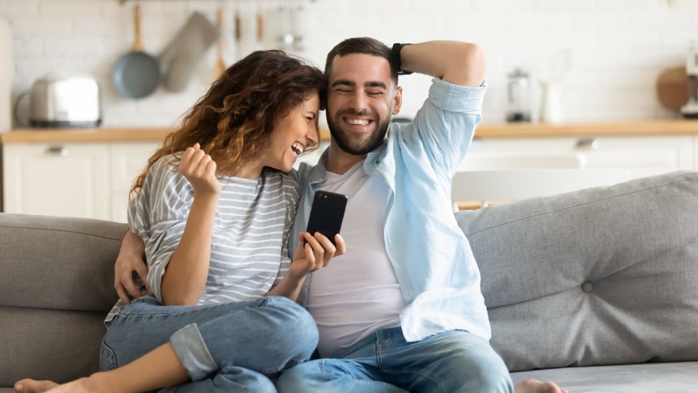 Male female couple cuddling on the couch looking at phone