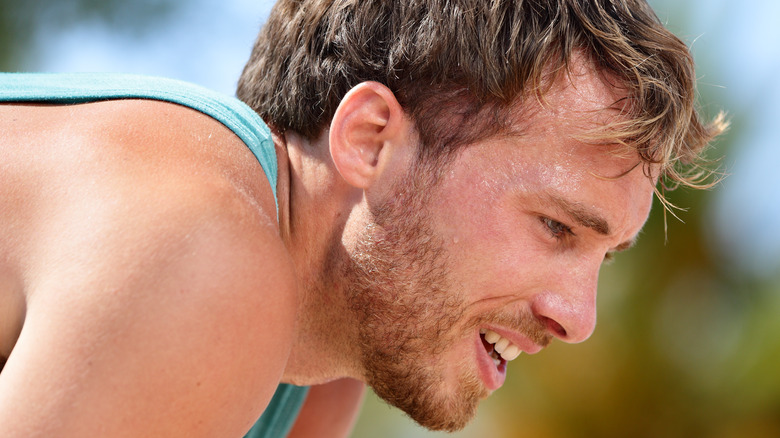 Male runner bending over with exhausted facial expression 